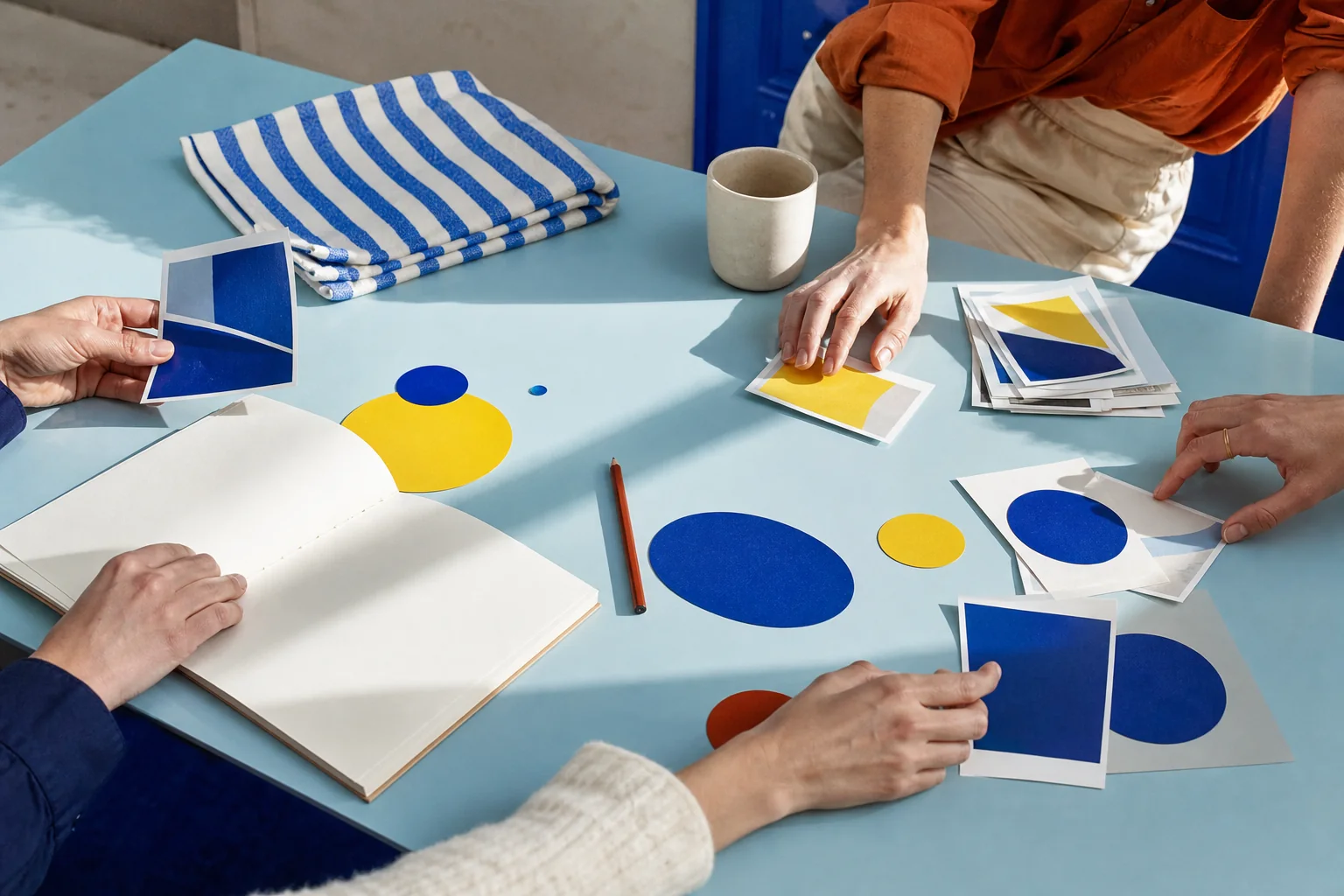 Une table éditoriale où plusieurs mains organisent notes et images